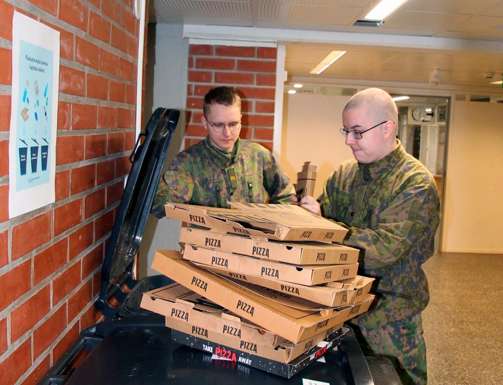 Kaksi varusmiestä laittaa tyhjiä pitsalaatikoita keräysastiaan.